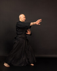 Portrait of aikido sensei master with black sensei belt in taekwondo kimono on black background....