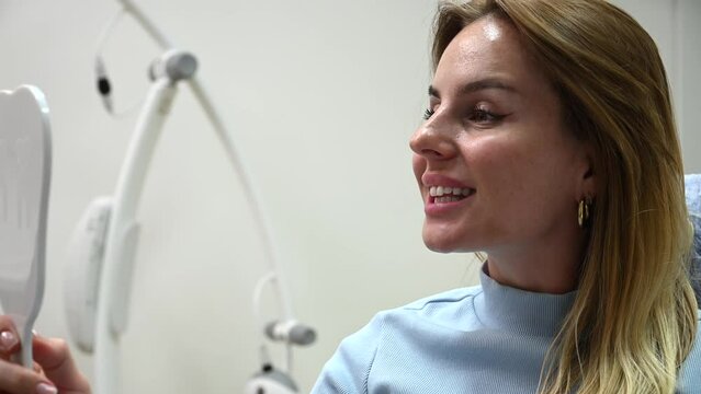Young Beautiful woman smile after Dental Whitening process smile in mirror. Teeth whitening with UF Lamp, Led Lamp and gel in Dental Clinic. 4k 120 fps slow motion Raw footage