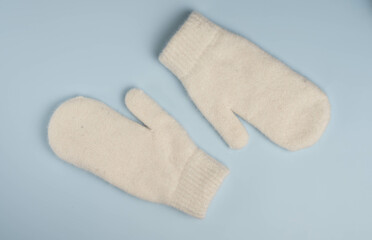 Warm white winter mittens on blue background. Top view, flat lay.