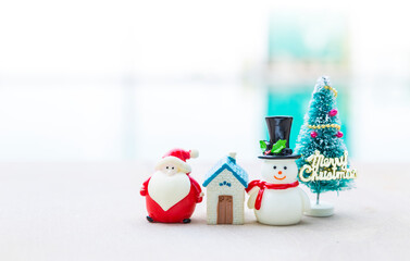 Miniature house and Santa Claus with Christmas tree and snowman on blurred background, outdoor day light, Happy Christmas background idea