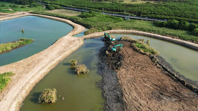 Excavator on muddy dirt island restores wetland in Guandu Nature park, aerial overview