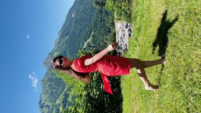 a girl in a red dress spins on green grass against the backdrop of mountains. High quality FullHD footage
