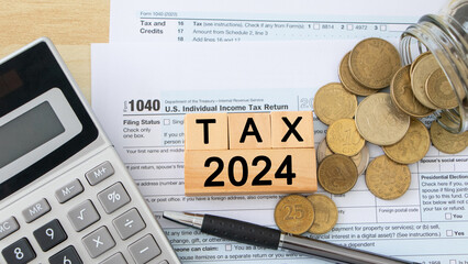 Word Tax 2024 in the wooden cube. US Individual income tax return. US tax forms and glass coin jar...