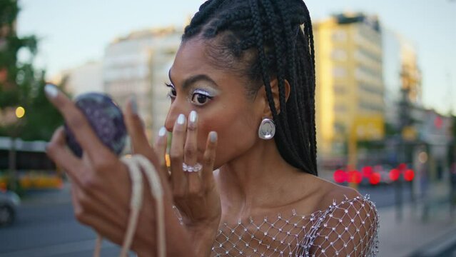 African model applying makeup at evening street closeup. Woman looking mirror