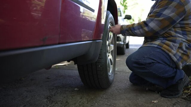 A Caucasian male checks the tire pressure on a red car.