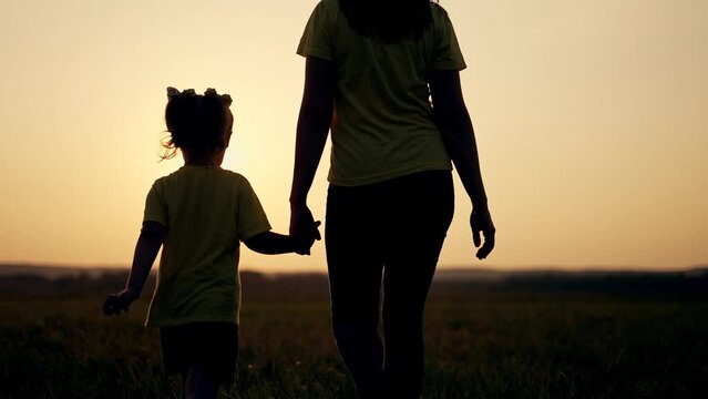 Happy family concept.Mom with baby is walk on grass in park.Mother with boy in field at sunset. Girl holds child by hand.Active lifestyle concept.Happy girl holds his mother by hand and walk on grass.