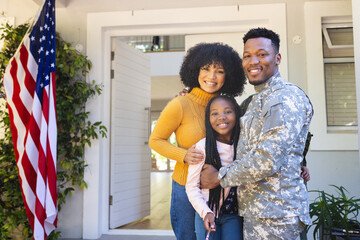 Portrait of happy african american family embracing outside home with usa flag, copy space