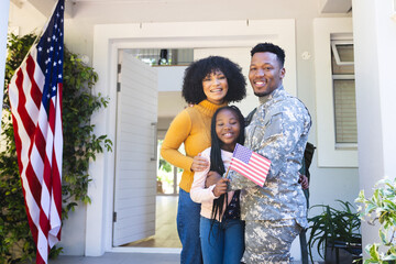Portrait of happy african american family embracing outside home with usa flag, copy space