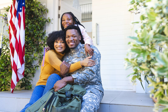 Portrait of happy african american family embracing outside home with usa flag, copy space