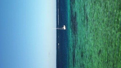 Sailboat in the crystal clear waters of New Caledonia - vertical aerial - Powered by Adobe