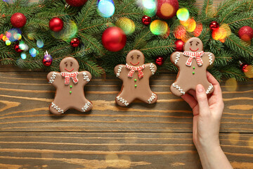 Female hand with Christmas gingerbread cookies and fir branches on wooden background, top view