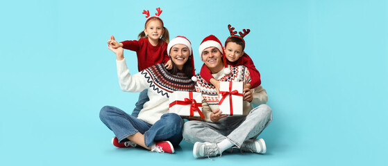 Happy family in Christmas clothes and with gifts on light blue background