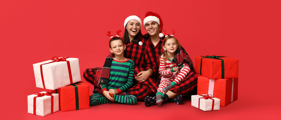 Fototapeta premium Happy family in Christmas pajamas and with gifts on red background