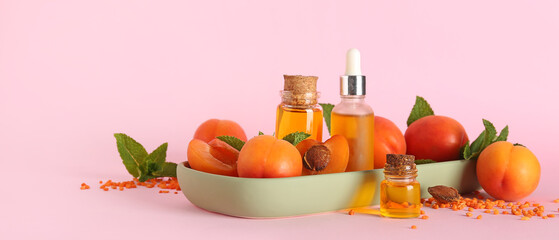 Bottles of essential oil, ripe apricots and sea salt on pink background
