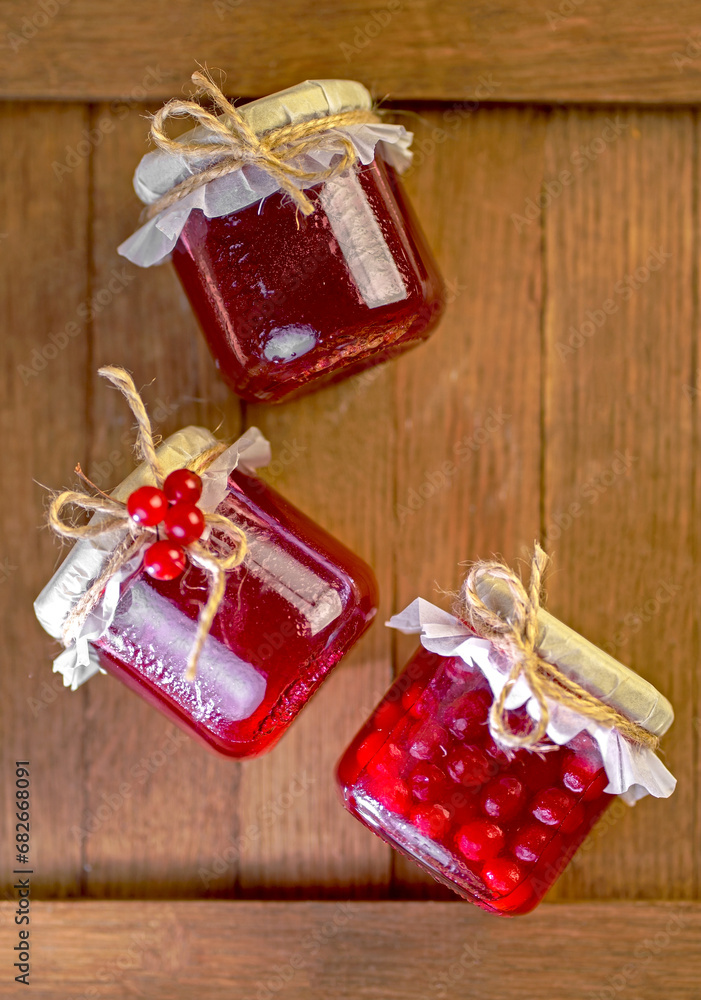 Poster viburnum jam. Red juicy berries of a viburnum with sugar in a glass jar on a dark wooden background. For making jam, tea. Medicinal plant.