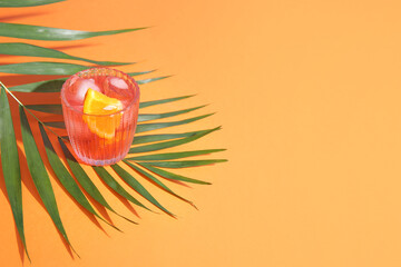 Glass of cold Negroni cocktail and palm leaf on color background