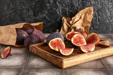 Wooden board and paper bag with fresh ripe figs on grey tile table