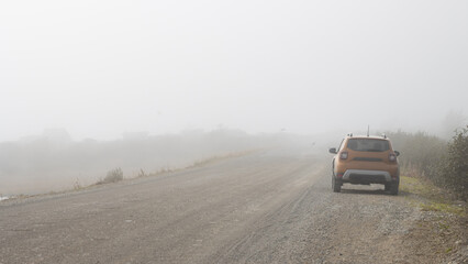 Naklejka premium Car on the side of a rural road. Poor visibility in fog. Foggy landscape.
