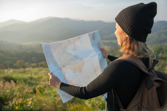 Adventurous girl navigating in with a topographic map in beautiful mountains of thailand. woman wearing hat stand alone and enjoying freedom and calm inspired travelling on background view mockup.