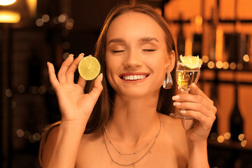 Young woman with tequila shot and lime in bar at night, closeup