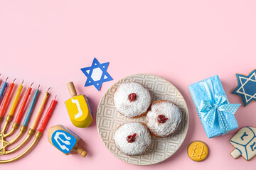 Menorah, dreidels, cookies, plate with donuts and gift box for Hanukkah celebration on pink...