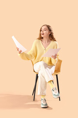 Beautiful actress with film script in chair on beige background