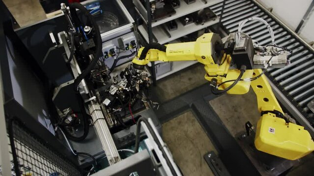 Automated robot arm moving and assembling metalic pieces in a factory.