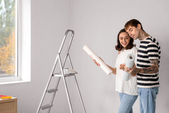 Young couple with wallpaper rolls doing repair in their new house