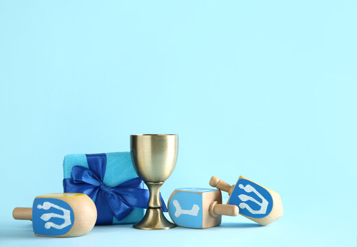 Dreidels with cup and gift box on blue background. Hanukkah celebration