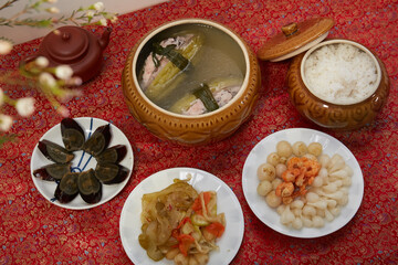 Family dinning table of Tet holiday or Lunar New Year with traditional foods: pork belly and eggs braised in coconut water, pickles, rice, Banh Tet (rice cake), fried vegetables, bitter melon soup