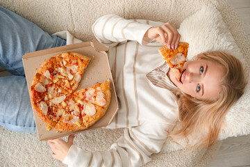 Young woman lying on couch and eating tasty pizza