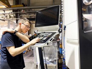 An inexperienced worker is looking for the right button to start working on a CNC milling machine