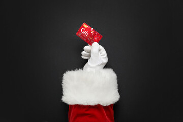 Santa Claus hand with gift card on dark background, closeup