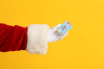 Santa Claus hand with gift card on yellow background, closeup