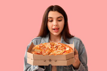 Young woman holding cardboard box with tasty pizza on pink background