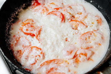 The process of cooking fish with tomatoes, close-up of melted cheese in a frying pan