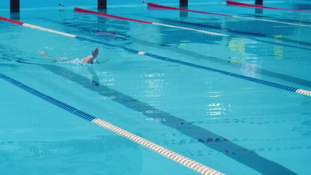 Woman athlete swimmer swims using backstroke technique in pool. Enjoying swimming and water sports.