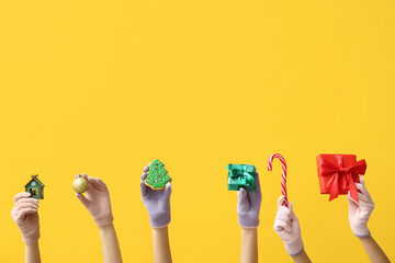 Female hands in warm gloves with Christmas decorations, gifts and sweets on yellow background