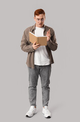 Emotional young man reading book on grey background