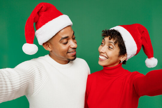 Close up merry young couple man woman wear red casual clothes Santa hat posing do selfie shot pov mobile cell phone isolated on plain green background. Happy New Year 2024 Christmas holiday concept.