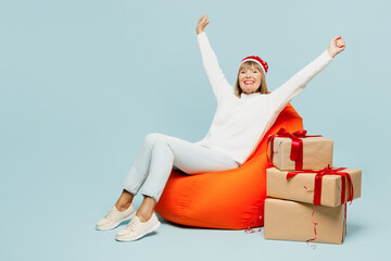 Full body merry elderly woman 50s years old wear sweater red hat posing sit in bag chair near stack...