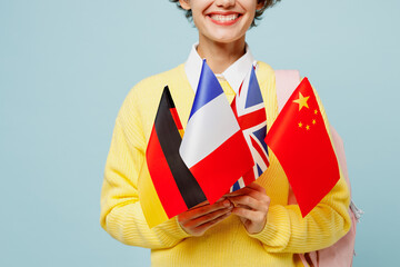 Fototapeta premium Close up cropped young smart smiling woman student wear casual clothes yellow sweater backpack bag hold in hands many flags isolated on plain blue background. High school university college concept.