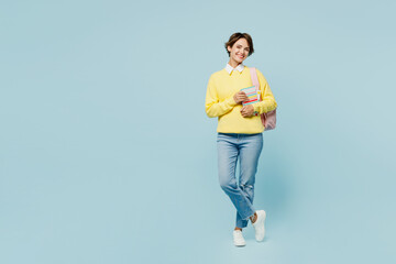 Full body young smiling happy cheerful cool fun woman student wear casual clothes sweater backpack bag hold books look camera isolated on plain blue background. High school university college concept.