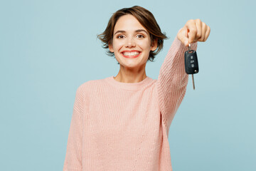 Young woman she wear beige knitted sweater casual clothes hold giving car key fob keyless system stretch hand to camera isolated on plain pastel light blue cyan background studio. Lifestyle concept.