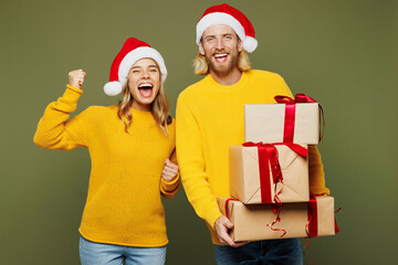 Merry young couple two friends man woman wear sweater Santa hat posing present box with gift ribbon bow do winner gesture isolated on plain green background. Happy New Year Christmas holiday concept.