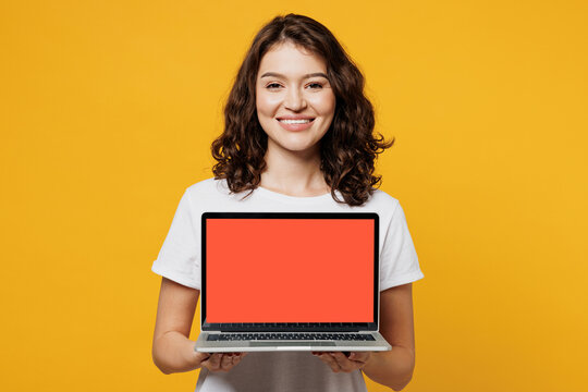 Young IT woman wears white blank t-shirt casual clothes hold use work on blank screen workspace area laptop pc computer isolated on plain yellow orange background studio portrait. Lifestyle concept.