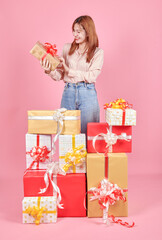 Photo of pretty adorable woman in pink shirt standing holding stack of gift boxes over pink studio background. celebrating women's day, valentine's, birthday, anniversary. shopping for holiday concept