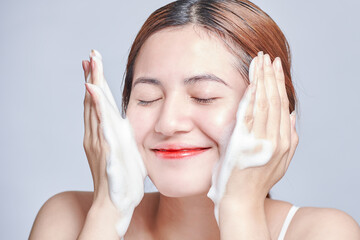 Smiling young woman washing foam face by natural foamy gel. satisfied girl with bare shoulders...