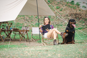woman and a rottweiler dog on a camping trip in nature. relaxing woman read a book sitting on...