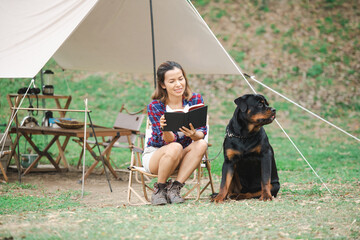 woman and a rottweiler dog on a camping trip in nature. relaxing woman read a book sitting on...
